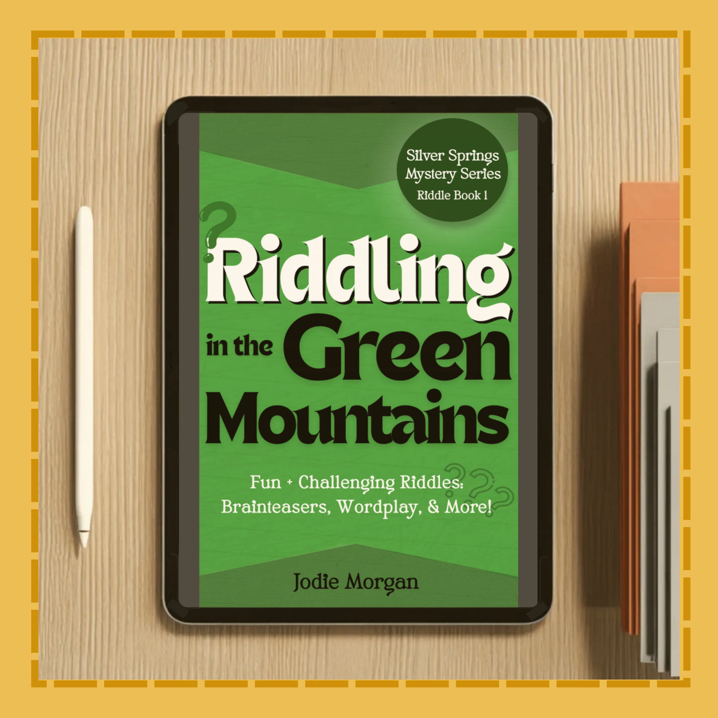 Digital book cover of 'Riddling in the Green Mountains' on a tablet with a pen and notebook on a wooden surface.