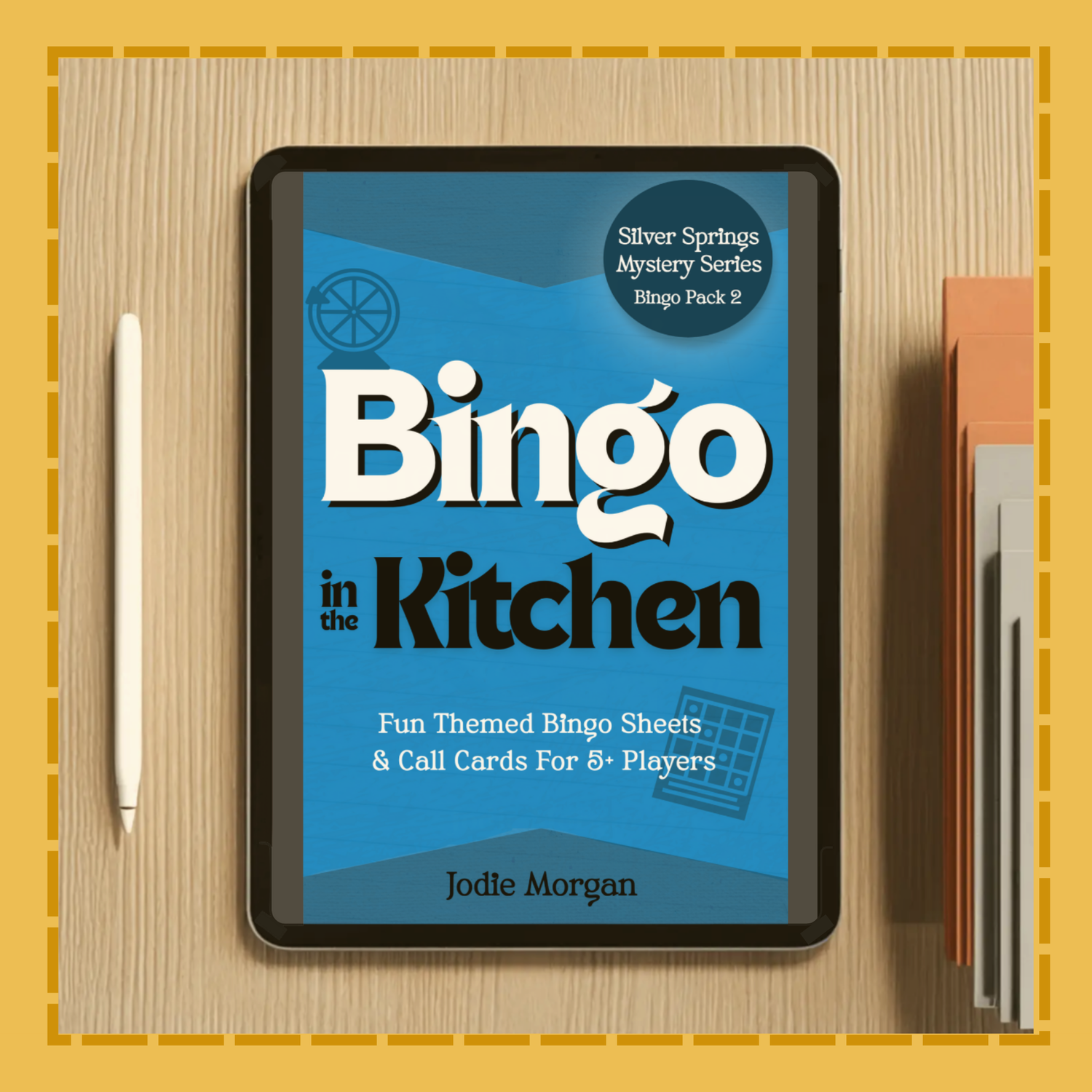 Tablet displaying 'Bingo in the Kitchen' book cover on a wooden surface with a pen and notebook.