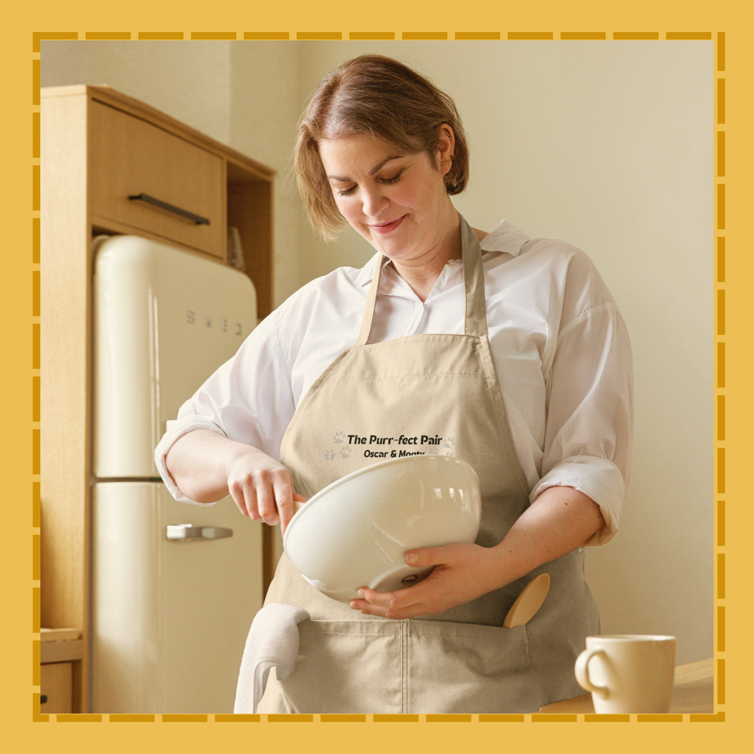 Woman in a kitchen wearing an apron with text, holding a white bowl.