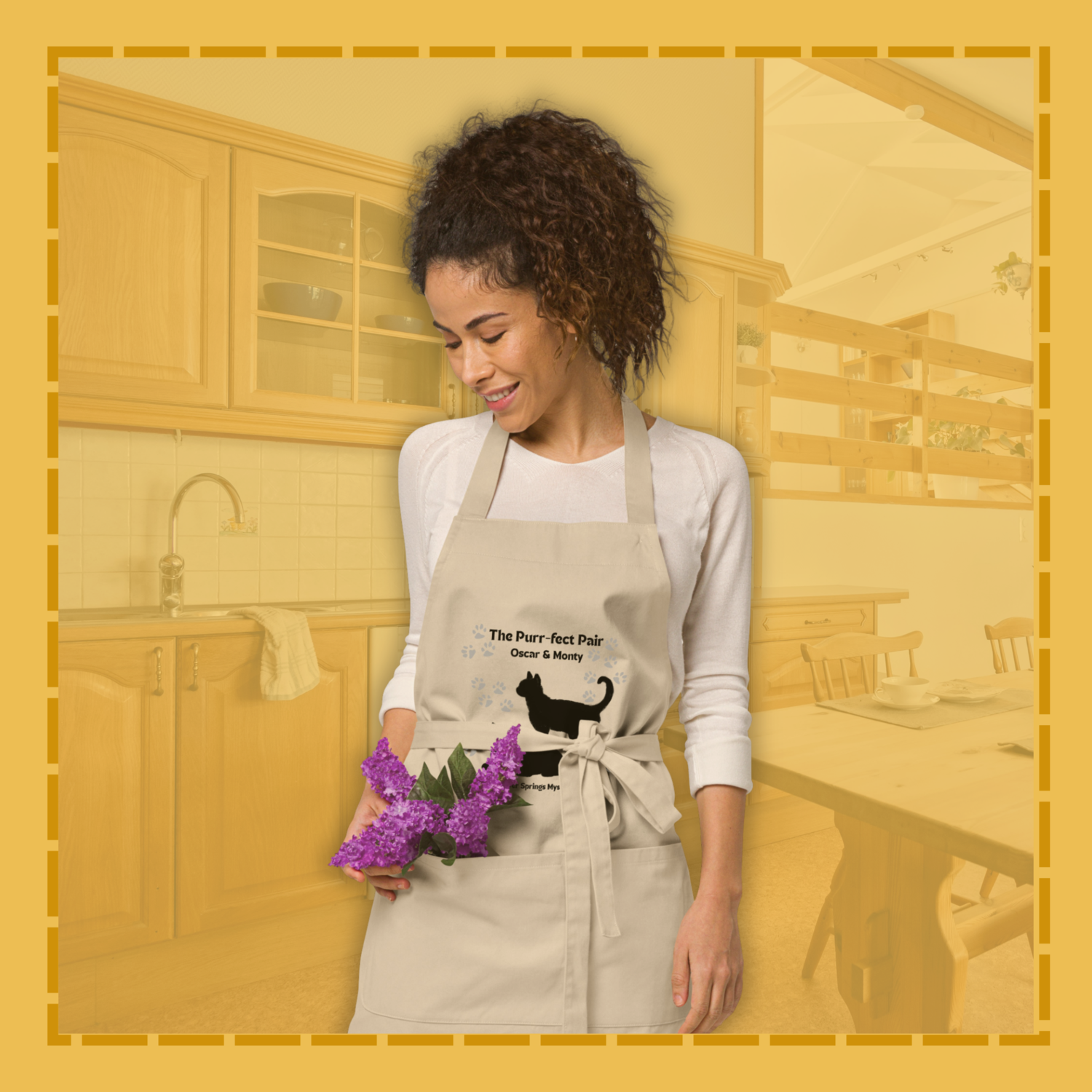 Woman wearing a kitchen apron with a cat design, holding flowers in a kitchen setting.