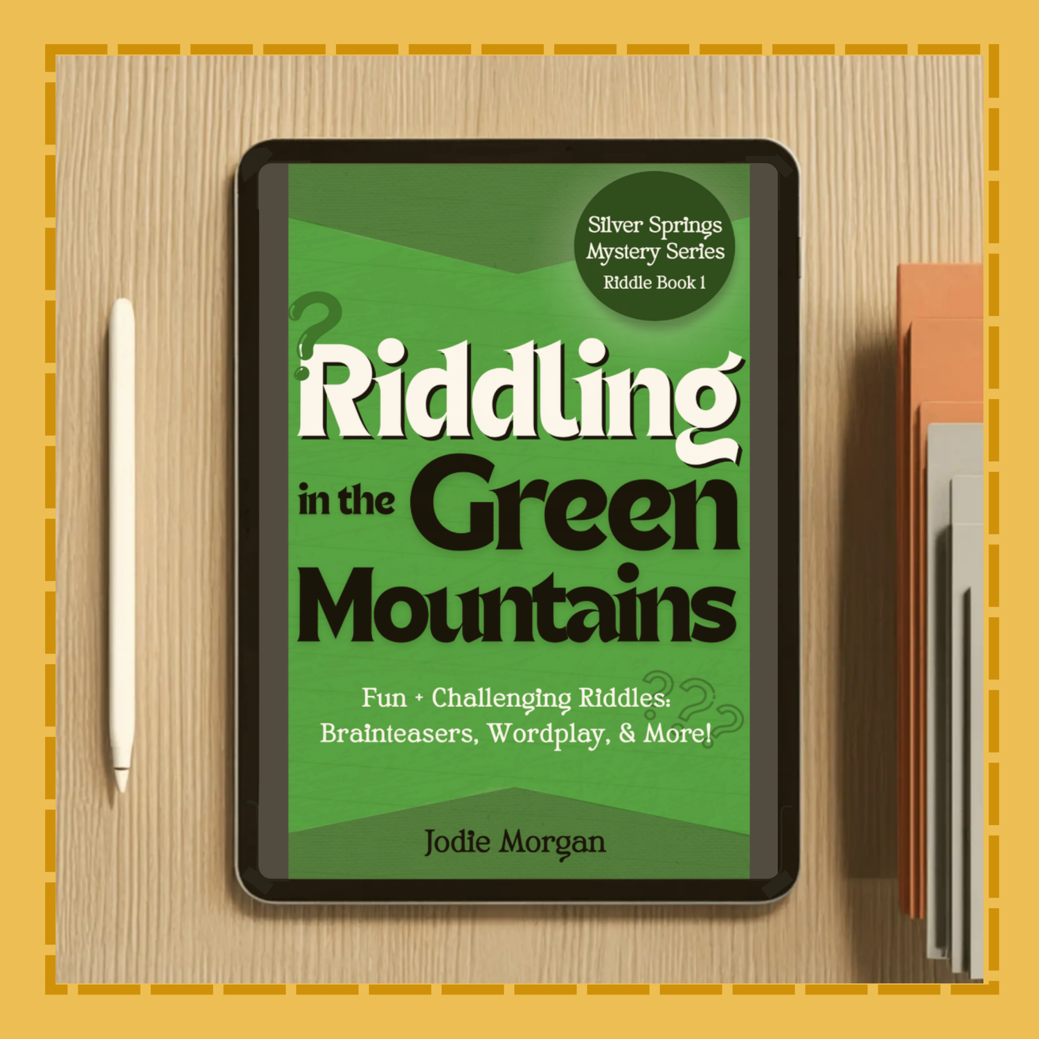 Digital book cover of 'Riddling in the Green Mountains' on a tablet with a pen and notebook on a wooden surface.